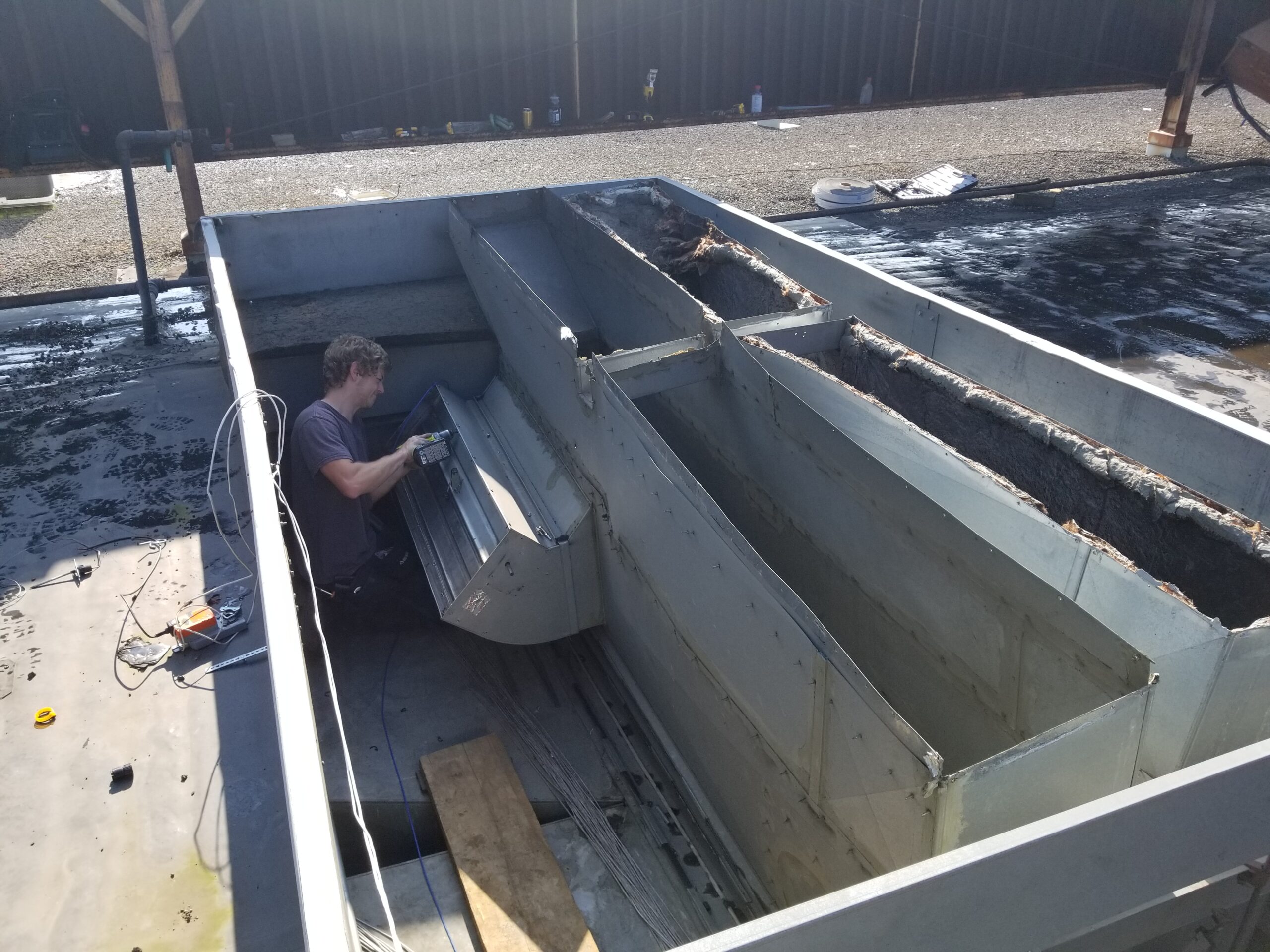 Technician working on a large sheet metal enclosure on a commercial roof