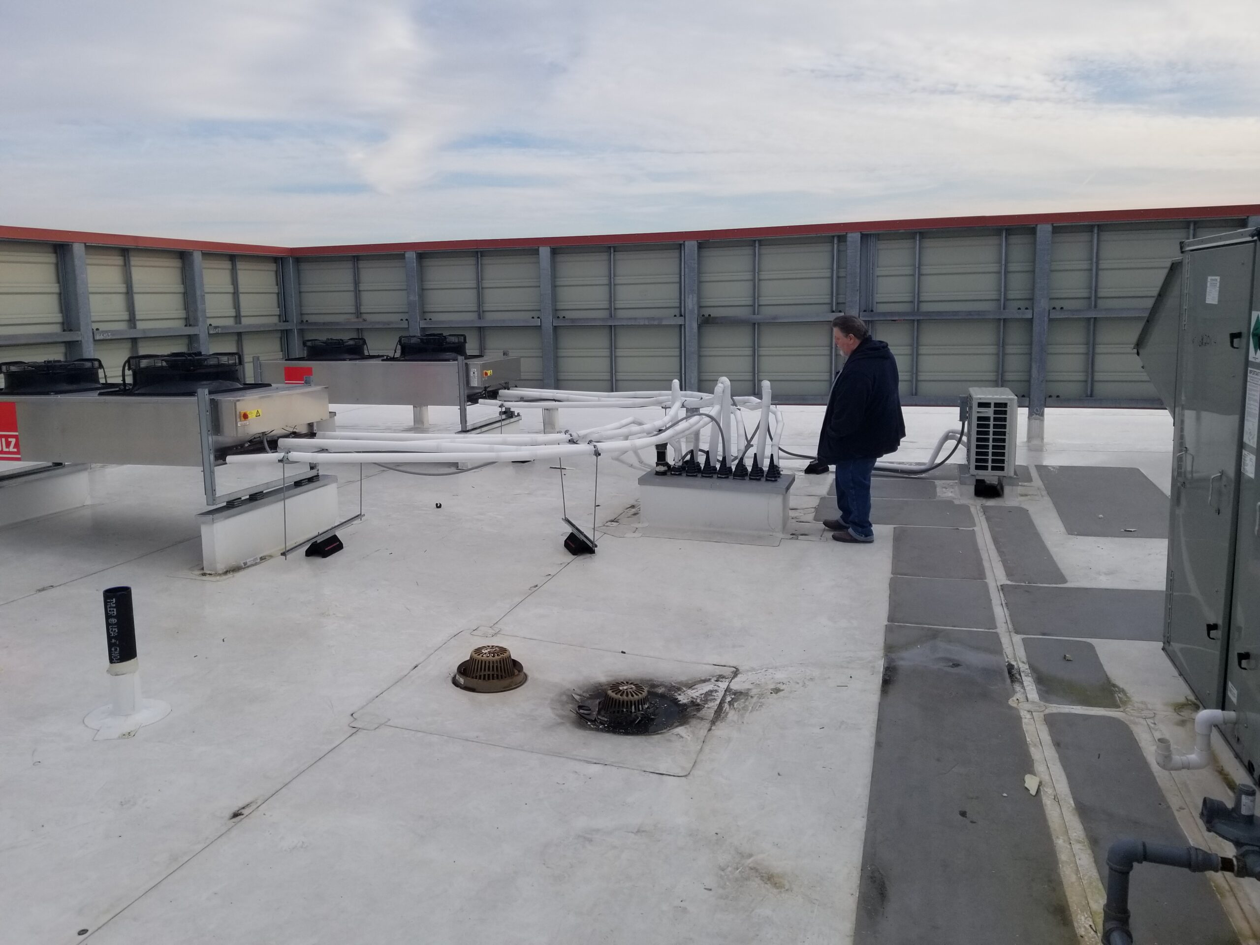 Technician on a flat commercial roof with piping and mechanical equipment