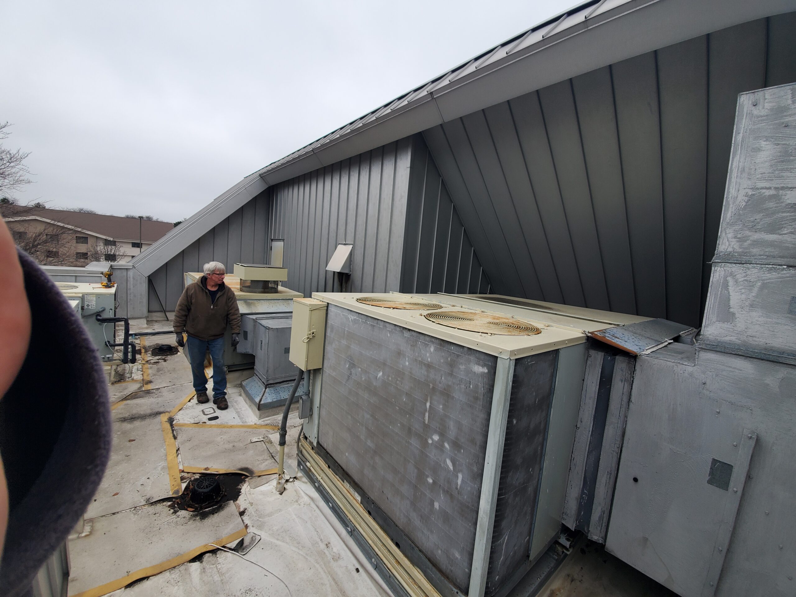 Crew member inspecting commercial rooftop equipment under an overcast sky